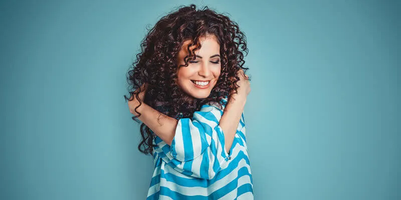 Woman with curly hair in a blue and white striped shirt hugs herself.