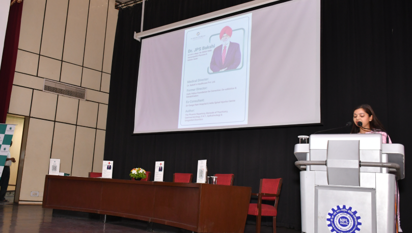 Speaker presenting Dr. Bakshi's profile at NPL.